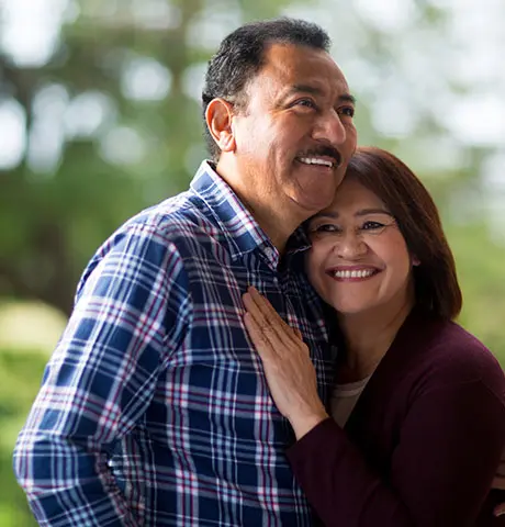 An older couple embraces and smiles while spending time outdoors.
