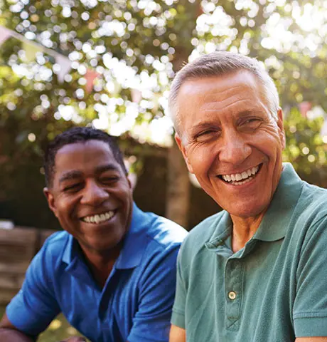 Two adult men smile while spending time outdoors on a sunny day.
