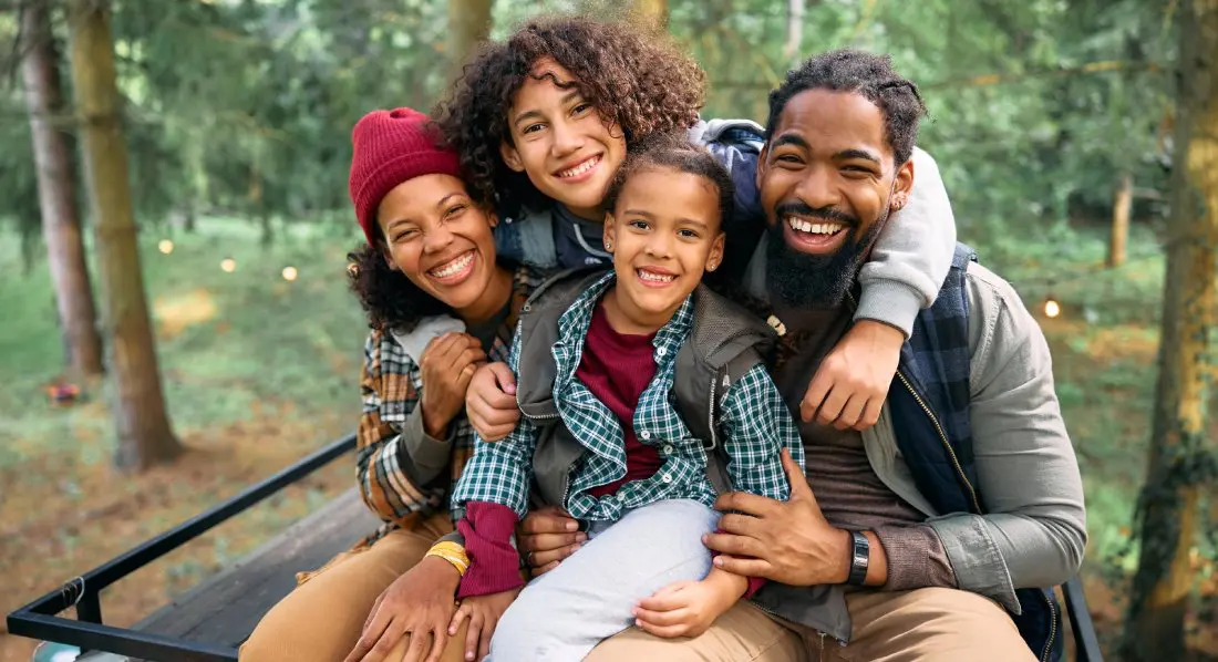 Happy African American parents with kids enjoying in camping at trailer park in the woods and looking at camera.